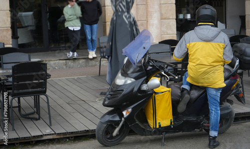 food delivery courier delivers food in city, town. Delivery courier motor scooter with yellow backpack. person near scooter is waiting for an order. restaurant. BATUMI, GEORGIA