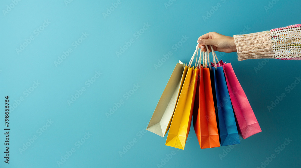 Woman's hand holds colored shopping bags on blue background. The concept of shopping and pleasant purchasing. With copy space