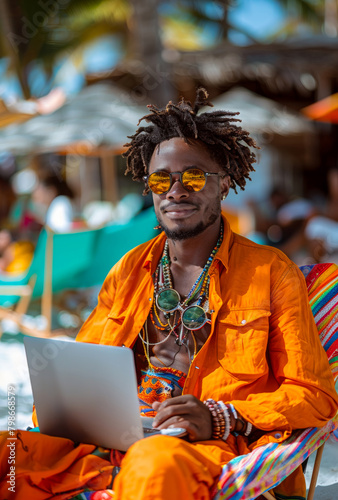 A cheerful black person, seated on a colorful beach chair, happily works on their laptop, with the backdrop of beac photo