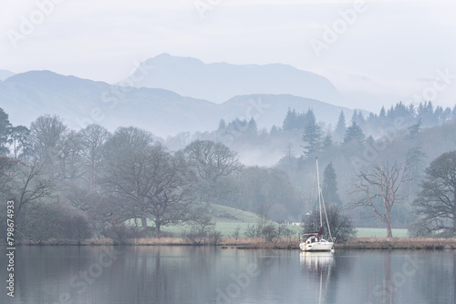 Stunning peaceful landscape image of misty Spring morning over Windermere in Lake District and distant misty peaks