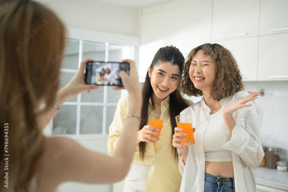 Two smiling women taking a selfie with orange drinks in a bright, modern kitchen, enjoying their time together. Two smiling women taking a selfie with orange drinks in a bright, modern kitchen, enjoying their time together.