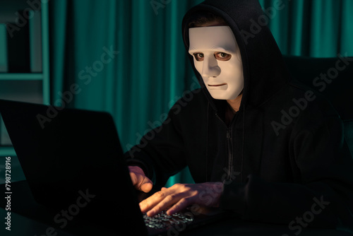 White criminal anonymous mask installing coding password encryption by programming hack, trying to make insecure thorough privacy taking massive database on computer for ransom to company. Pecuniary.
