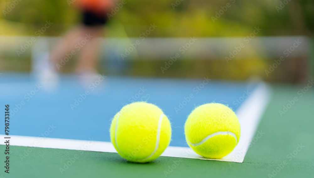 tennis balls on white line of green and blue hard court with blurred court and player as background