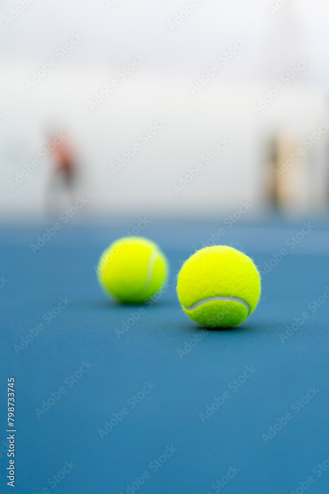 two tennis balls on blue tennis court, selective focus, blurred player and as background