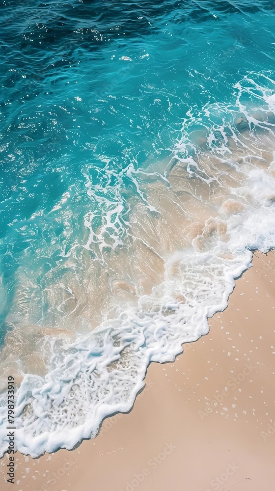Top view of a sandy beach with clear blue water, waves, and a coastline, perfect for summer themes