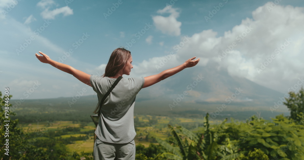 A woman standing a top a vibrant green hillside overlooking a scenic landscape. The hillside is rich with vegetation under the blue skies. A woman standing a top a vibrant green hillside overlooking a scenic landscape. The hillside is rich with vegetation under the blue skies.