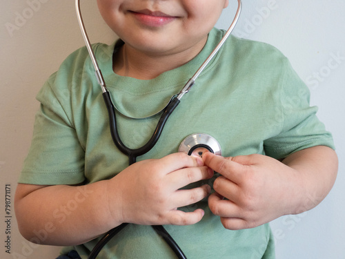 fat kid put green tight shirt listens to the lungs and heart with medical stethoscope. hospital life insurance concept, World heart health day, doctor day, world hypertension day.