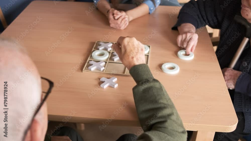 Senior friends playing tic tac toe at table in nursing home