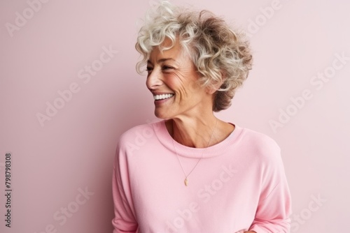 Portrait of a happy senior woman laughing against a pink background.