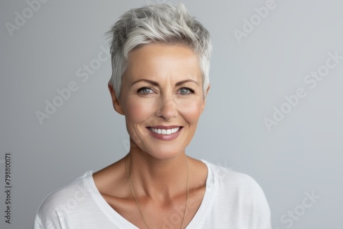 Mature woman with short grey hair. Beautiful mature woman smiling and looking at camera while standing against grey background