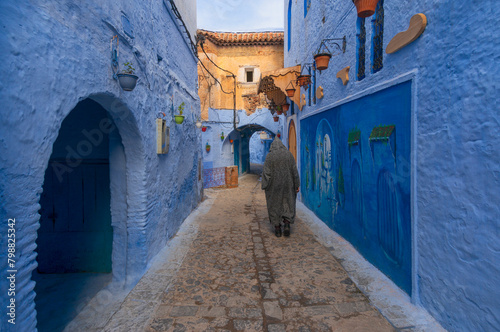 Man walking on narrow street in medina of blue city, Chefchaouen. Man wearing traditional clothes (Moroccan Djellaba), One of the most popular forms in Morocco.  © DOCKSTUCK