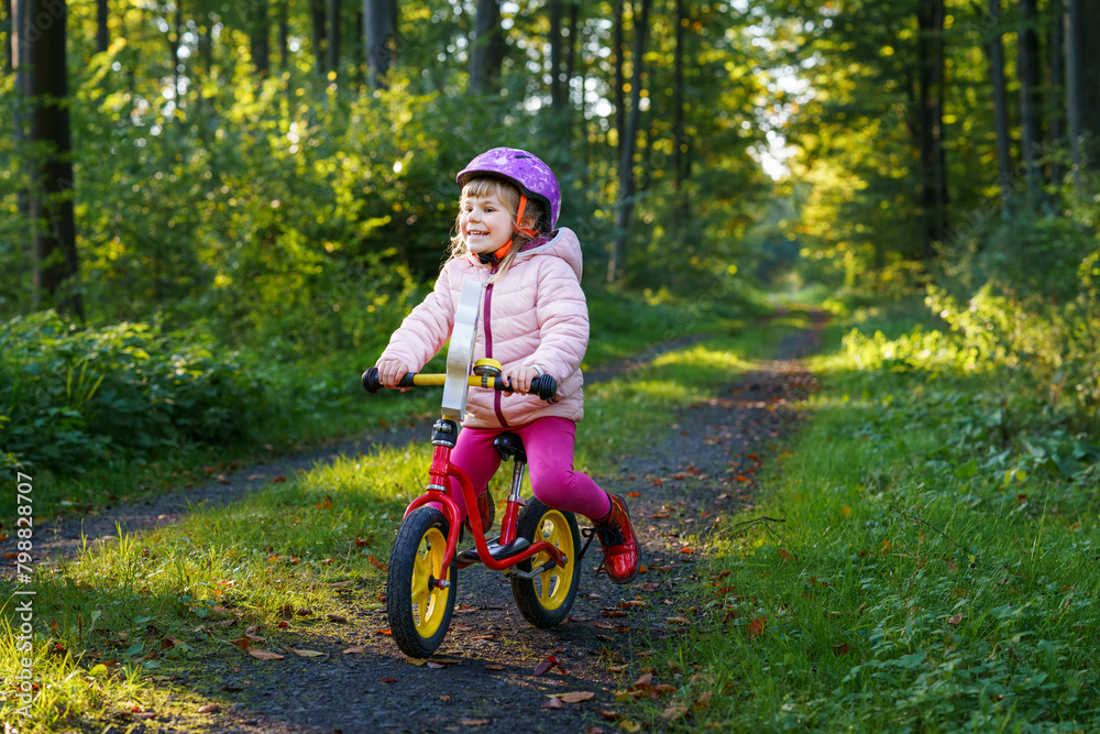 Child riding balance bike. Kids on bicycle in sunny forest. Little girl enjoying to ride glider bike on warm day. Preschooler learning to balance on run bicycle in safe helmet. Sport activity Child riding balance bike. Kids on bicycle in sunny forest. Little girl enjoying to ride glider bike on warm day. Preschooler learning to balance on run bicycle in safe helmet. Sport activity