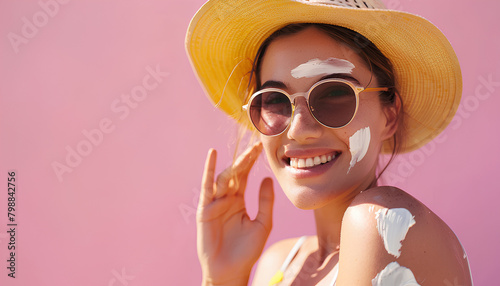 Young woman applying sunscreen cream on pink background photo
