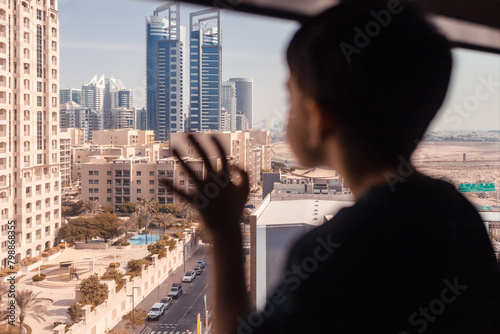 Lonely boy looking out through the window. Dubai buildings in the back