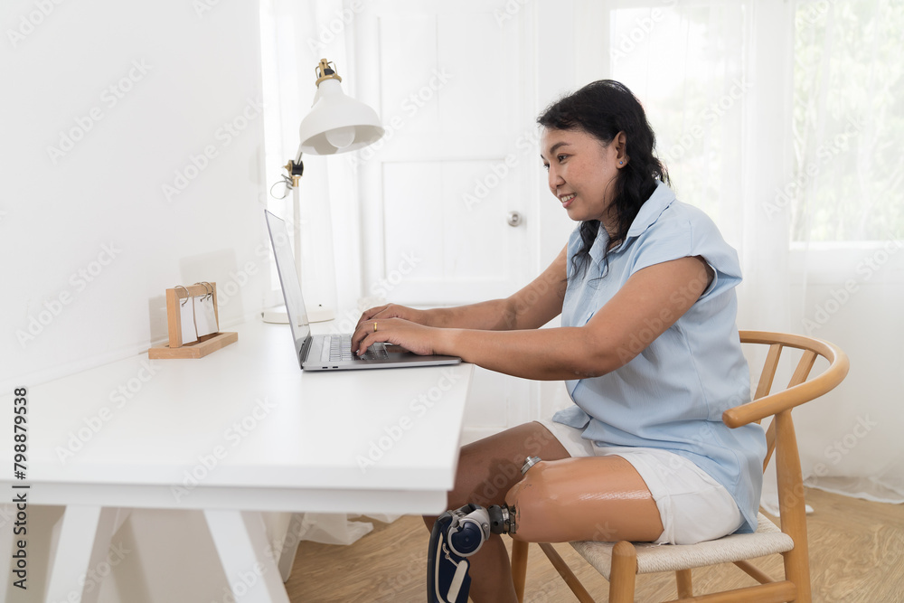 Asian woman with prosthetic leg using laptop computer at home. Woman with prosthetic leg working at home Asian woman with prosthetic leg using laptop computer at home. Woman with prosthetic leg working at home
