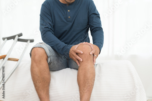 Man touching knee during sitting on sofa at home. Knee pain. Knee ache concept