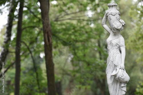 sculpture of a girl in the spring park. An old statue in a park of a semi-nude Greek or Italian Renaissance woman with a vase in a city park. in the summer garden. 