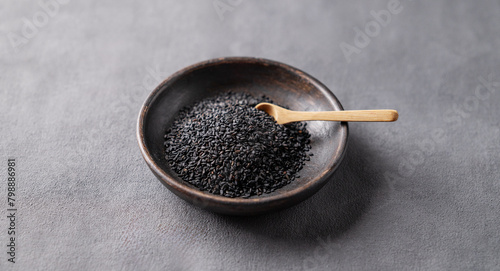 Black sesame seeds in a wooden bowl on a dark background.