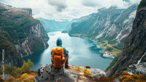 Traveler with backpack gazes at lake from rock in natural landscape