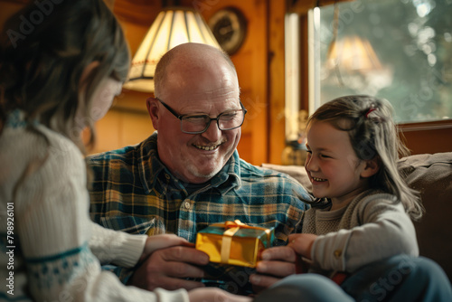 A man with glasses smiles joyfully, hugging two young children who hold a gift