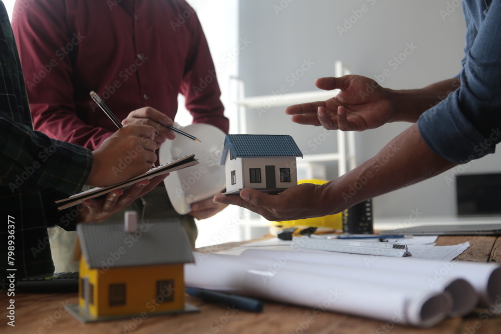 Engineers are consulting the team to design an architectural structure for clients with blueprints and building models to work at office. Engineers are consulting the team to design an architectural structure for clients with blueprints and building models to work at office.
