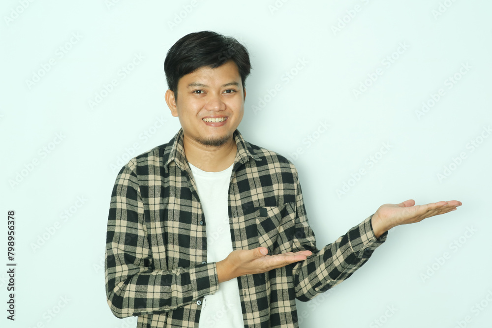 Young Asian man wearing brown flannel shirt smiling while pointing with his open palm Young Asian man wearing brown flannel shirt smiling while pointing with his open palm