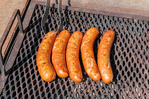 Big yummy sausages are being grilled outdoors on a warm sunny day
