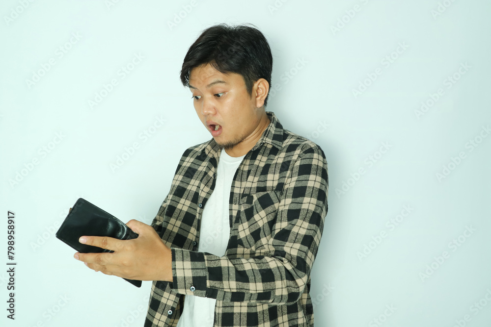 Young Asian man looks at his empty wallet with a shocked expression. Side view Young Asian man looks at his empty wallet with a shocked expression. Side view