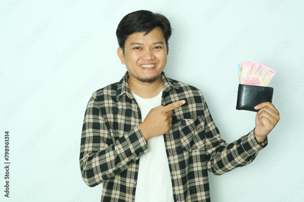 Young Asian man wearing a brown flannel shirt pointed his right finger at the wallet full of money and smile.