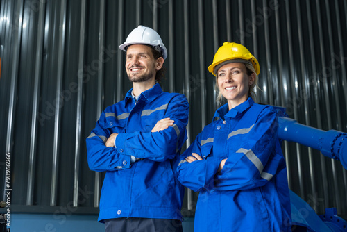Two professional engineers in hard hats and blue workwear standing confidently in an industrial facility with arms crossed.