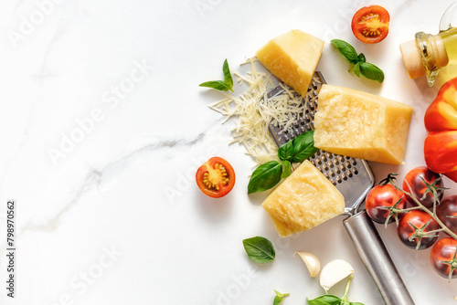 Italian food cooking ingredients background with fresh cherry tomatoes, basil leaves, herbs, garlic, olive oil and parmesan cheese on white stone table with copy space top view. Healthy eating