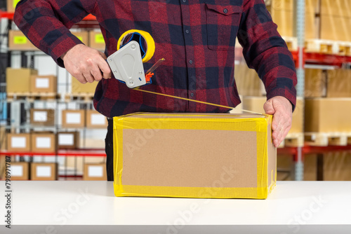 Man will pack box. Packer guy uses dispenser with tape. Packing parcel at warehouse. Cropped packer at work. Wrapping cardboard box with tape. Person works as packer in distribution center