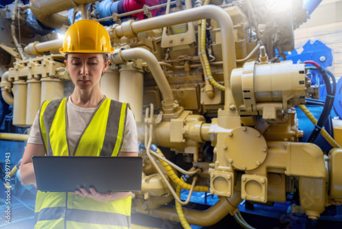 Woman industrialist. Girl with laptop in factory building. Ship engine. Female employee of shipbuilding enterprise. Woman industrialist stands with computer. Engineer designs ship engines photo