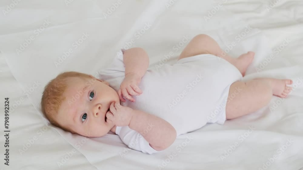 newborn baby boy smiling on a white bed at home, family with a small child, close-up, place for text, cute baby sucking pens. newborn baby boy smiling on a white bed at home, family with a small child, close-up, place for text, cute baby sucking pens.