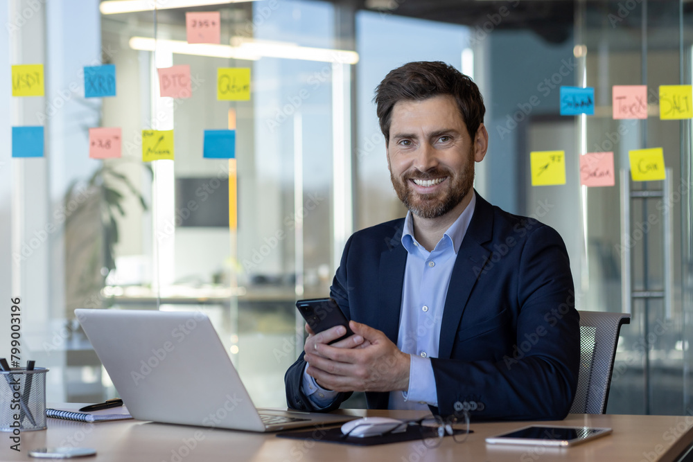 Portrait of successful man in business suit in office interior, mature businessman smiling and looking at camera, satisfied with achievement results, using app on phone. Portrait of successful man in business suit in office interior, mature businessman smiling and looking at camera, satisfied with achievement results, using app on phone.