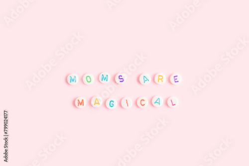 Moms are magical. Quote made of white round beads with multicolored letters on a pink background. © rorygezfresh