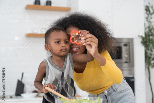 African American young mother cooking with little son in kitchen room at home photo