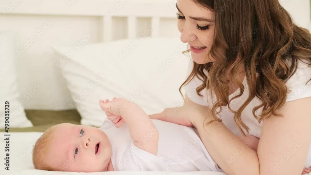mom with a newborn baby boy at home on the bed, a young mother admires and plays with the baby, smiles and rejoices kissing his legs mom with a newborn baby boy at home on the bed, a young mother admires and plays with the baby, smiles and rejoices kissing his legs
