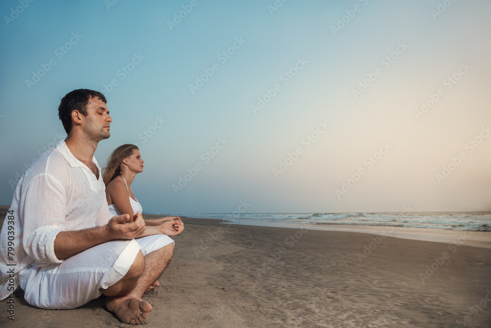 Young couple relaxing on sandy beach near colorful boat during sunset.