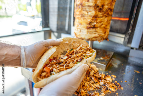 turkish chicken doner kebab sandwich in the hands of the chef with rotisserie on background