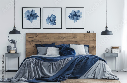 A Scandinavian style bedroom with white walls, a wooden headboard and bed frame, blue accents on the blanket, pillows and posters hanging above it