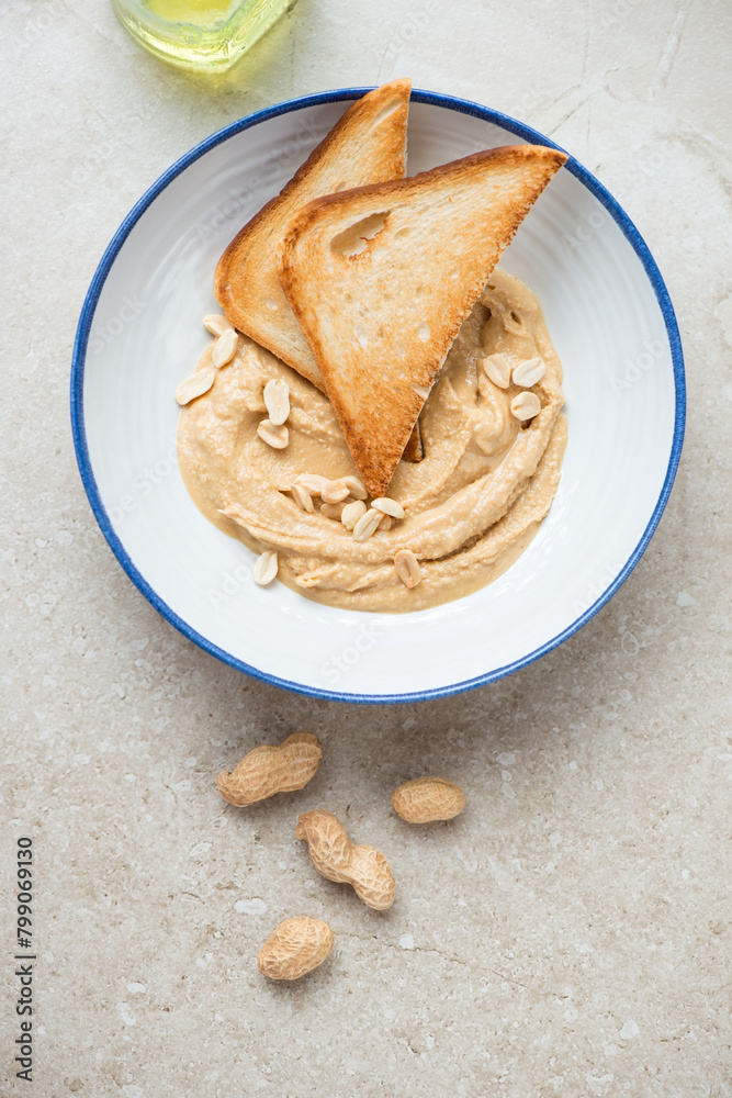 Blue and white plate with peanut butter and toasts, vertical shot on a beige stone background, above view Blue and white plate with peanut butter and toasts, vertical shot on a beige stone background, above view