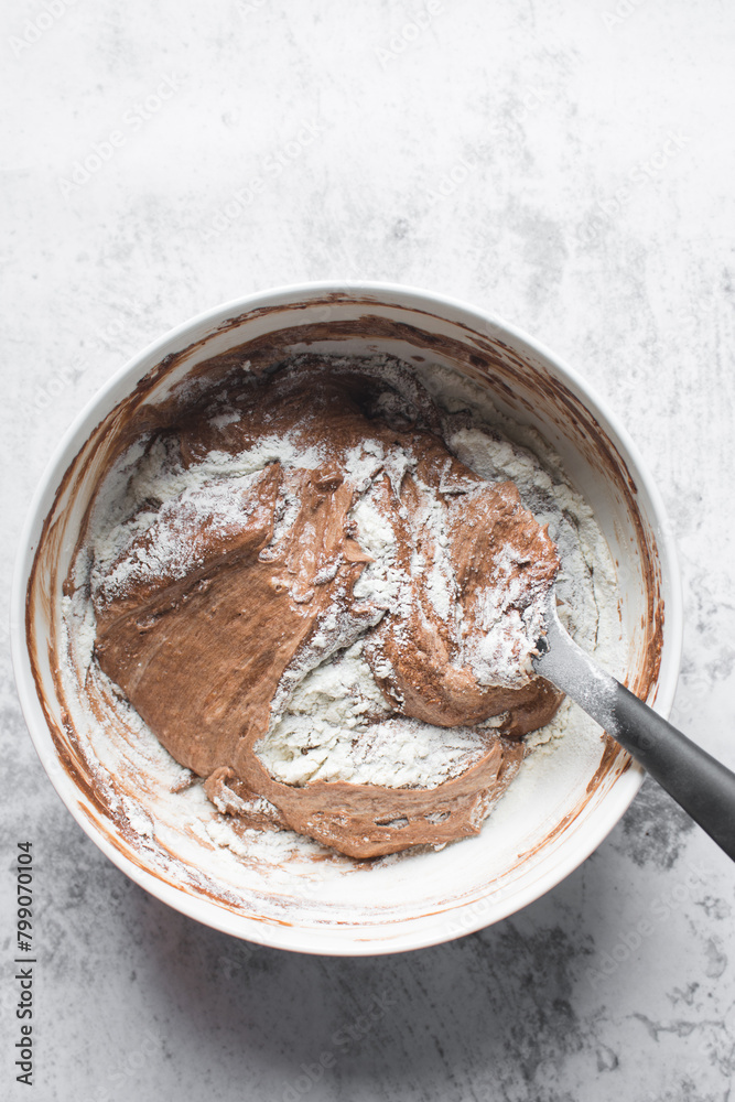Chocolate cake batter being mixed in a white bowl, folding cake batter in a white mixing bowl, the process of making chocolate cake Chocolate cake batter being mixed in a white bowl, folding cake batter in a white mixing bowl, the process of making chocolate cake
