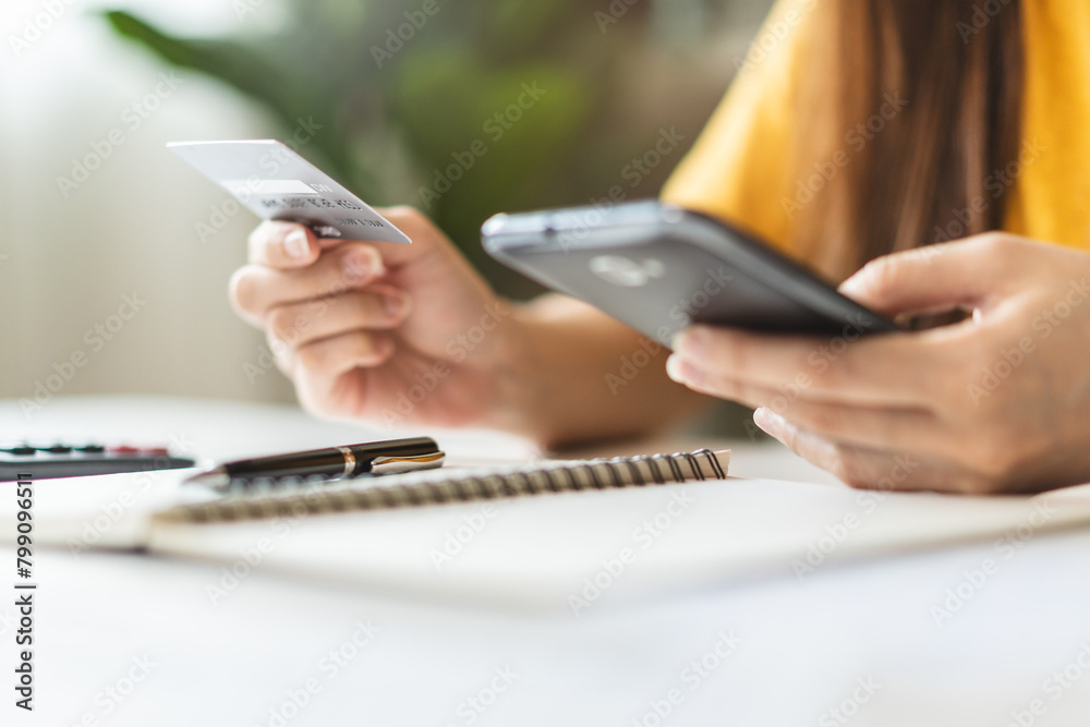 Fototapeta premium Close up view hands of young woman holding a credit card and doing bank transactions via mobile phone application at home