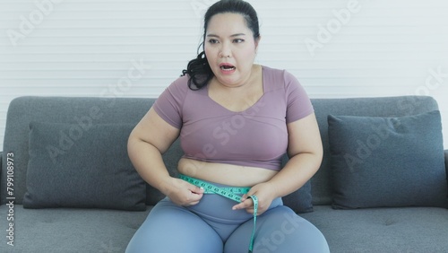 chuuby woman sitting on sofa using tape to measure her waist circumference