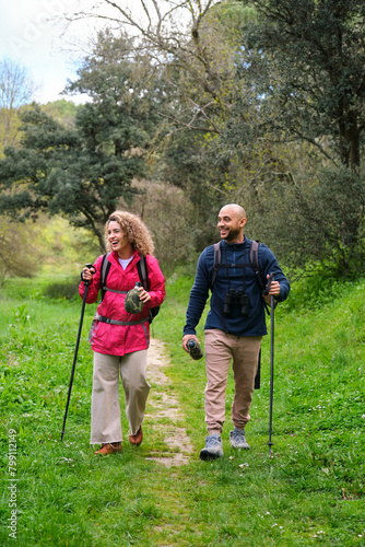 A man and a woman are walking in a forest. Trekking and hiking. They are both carrying backpacks and walking sticks.