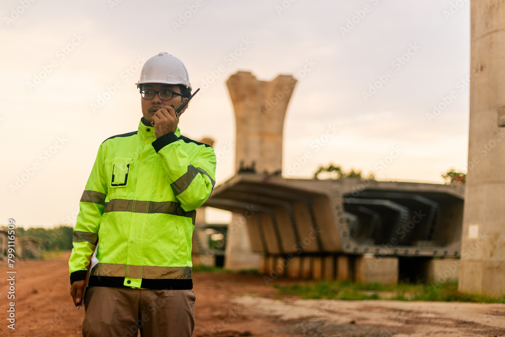 A man in a yellow jacket is writing on a clipboard while standing in front of a bridge. Concept of work and productivity A man in a yellow jacket is writing on a clipboard while standing in front of a bridge. Concept of work and productivity