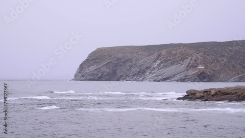 A rocky shoreline with a large body of water in the background. The water is choppy and the sky is overcast