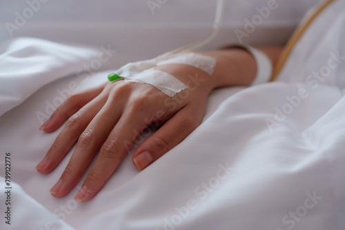 Close-up of an adult hand with IV line, soft focus on white linen, conveying a sense of medical care and patient recovery.