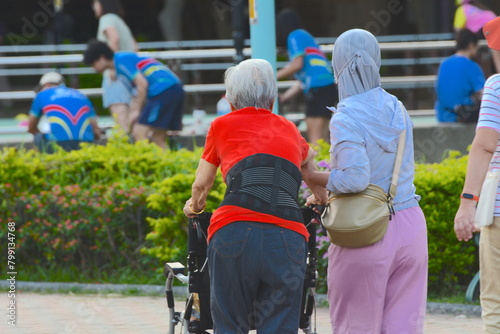 A maid supports an elderly person pushing a wheelchair